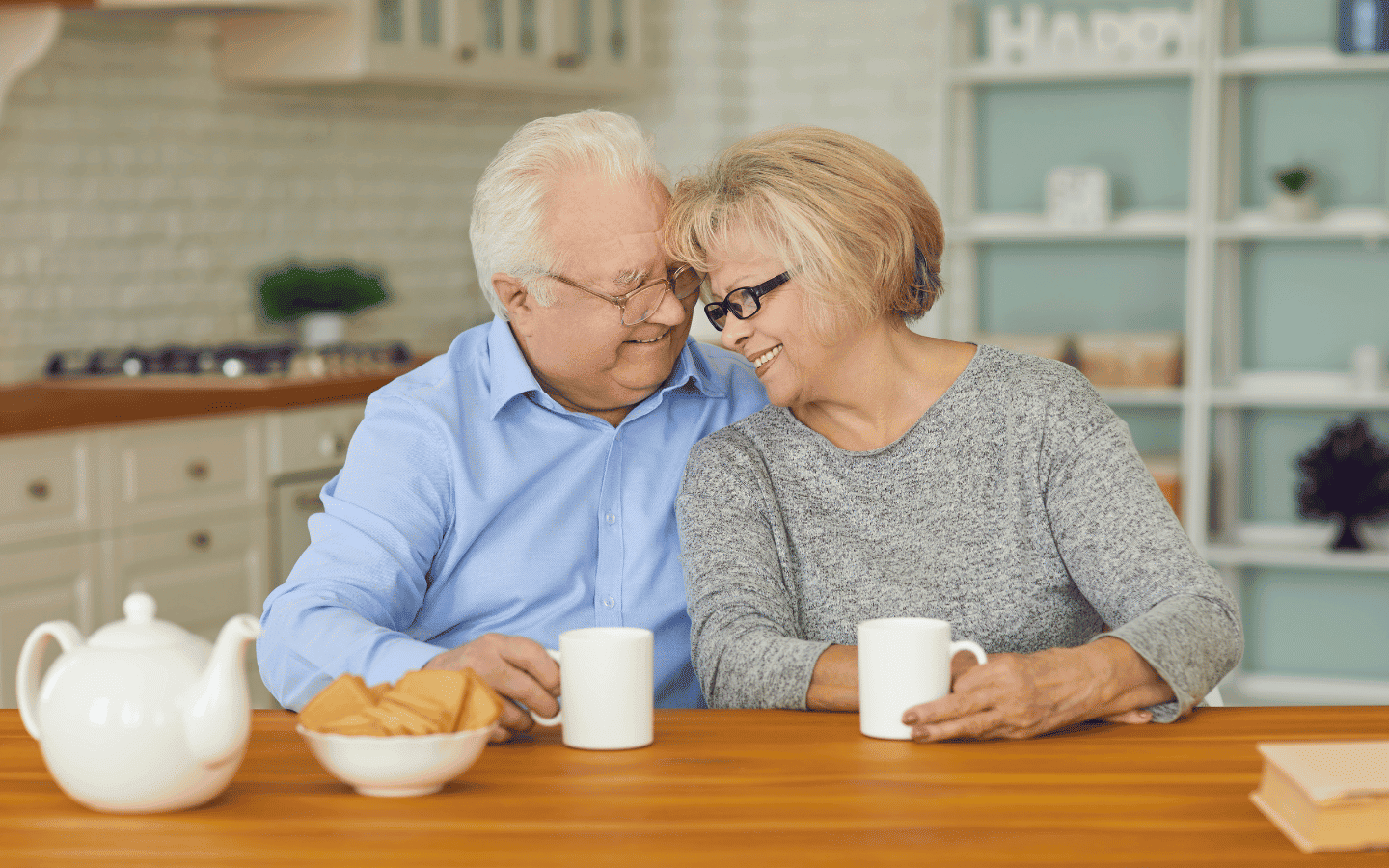 Pareja mayor compartiendo una taza de té en la cocina de su hogar.